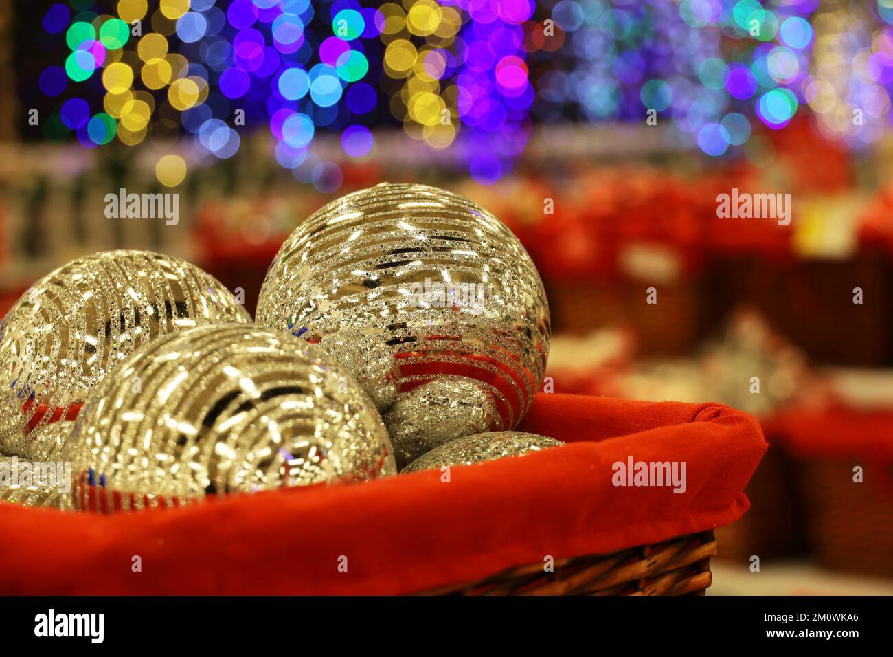 Weihnachtsspielzeug, goldene Kugeln in rotem Korb auf verschwommenem festlichem Hintergrund. Neujahrsdekoration in einem Geschäft Stockfoto
