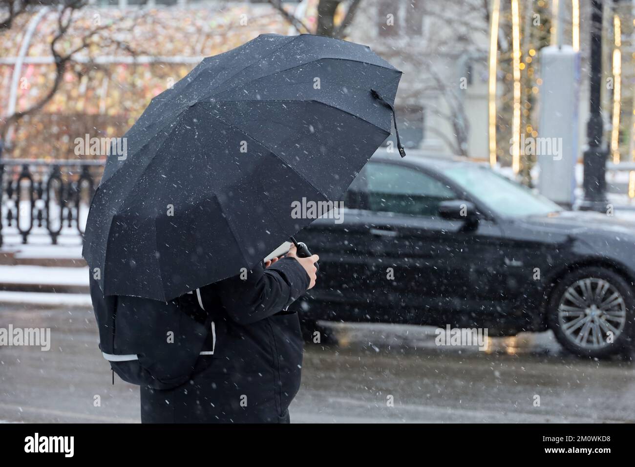 Schnee mit Regen in der Winterstadt, Frau mit Schirm steht auf einer Straße im Autohintergrund Stockfoto