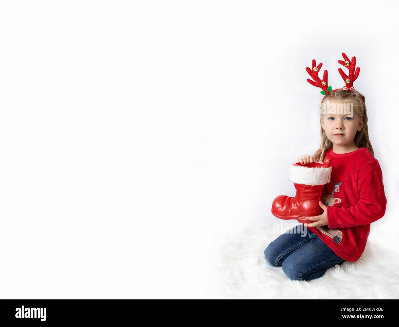 Weihnachten. Ein Mädchen mit Hirschhörnern in einem roten Pullover hält weihnachtsmannstiefel. Banner Stockfoto