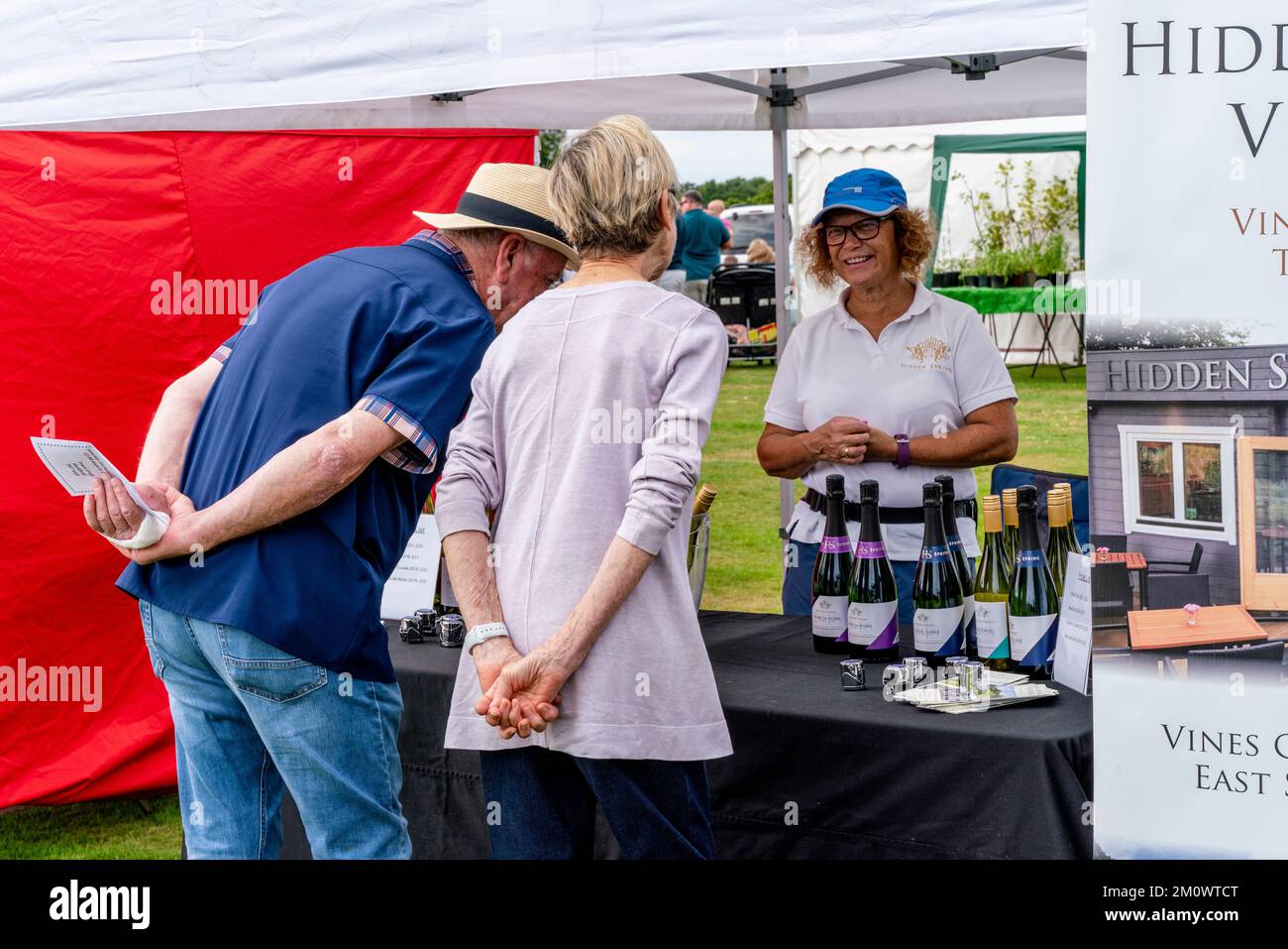 Ein Seniorenpaar schaut Auf Eine Weinausstellung vom Hidden Spring Vineyard, Hartfield Village Fete, Hartfield, East Sussex, Großbritannien. Stockfoto