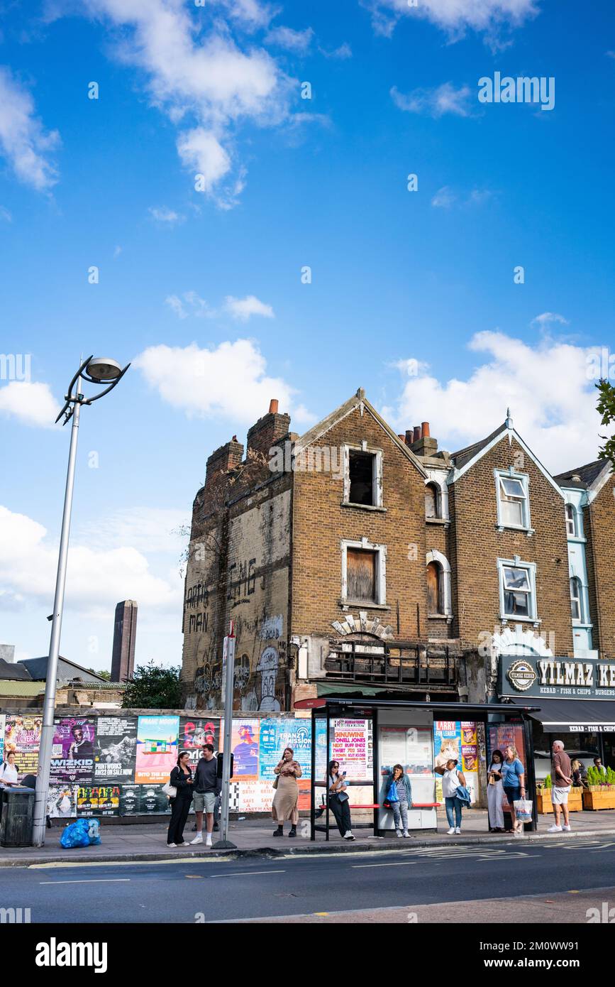 Peckham Rye in Süd-London, England, Großbritannien, mit ausgebranntem Gebäude und Menschen, die unter blauem Himmel an der Bushaltestelle warten Stockfoto