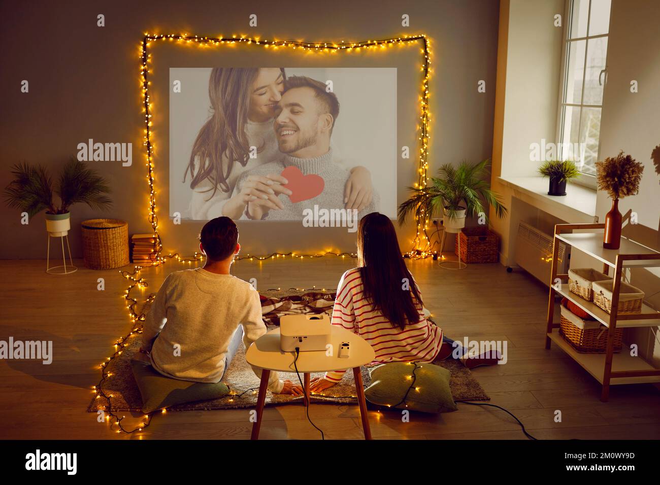 Ein Paar, das zu Hause ein Valentinsdate hat, einen Projektor verwendet, einen Film oder Fotos anschaut Stockfoto