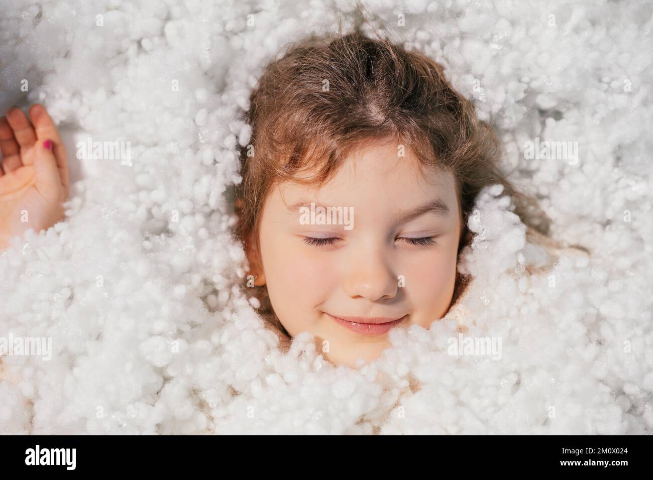 Schließen Sie ein ruhiges, lächelndes Mädchengesicht mit geschlossenen Augen in weißer, weicher Baumwollfeder. Gut geschlafen, tiefer Schlaf Stockfoto