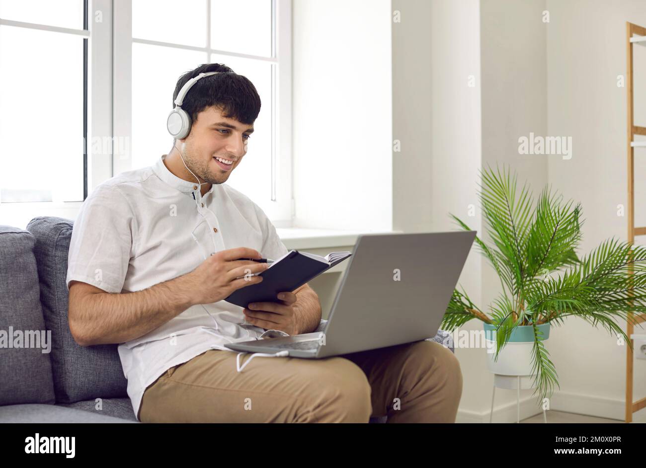 Glücklicher junger Mann, der seinen Laptop-Computer benutzt, um an Online-Kursen in Fremdsprache teilzunehmen Stockfoto Glücklicher junger Mann, der seinen Laptop-Computer benutzt, um an Online-Kursen in Fremdsprache teilzunehmen Stockfoto