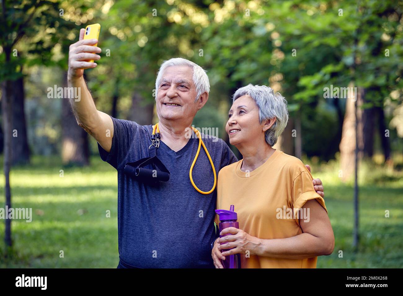 Altes sportliches Paar starrt auf Smartphone-Kamera Selfie-Foto machen Genießen Sie die moderne Nutzung von Wireless-Technologie, während Sie in Sportkleidung im Sommerpark spazieren. Carefre Stockfoto