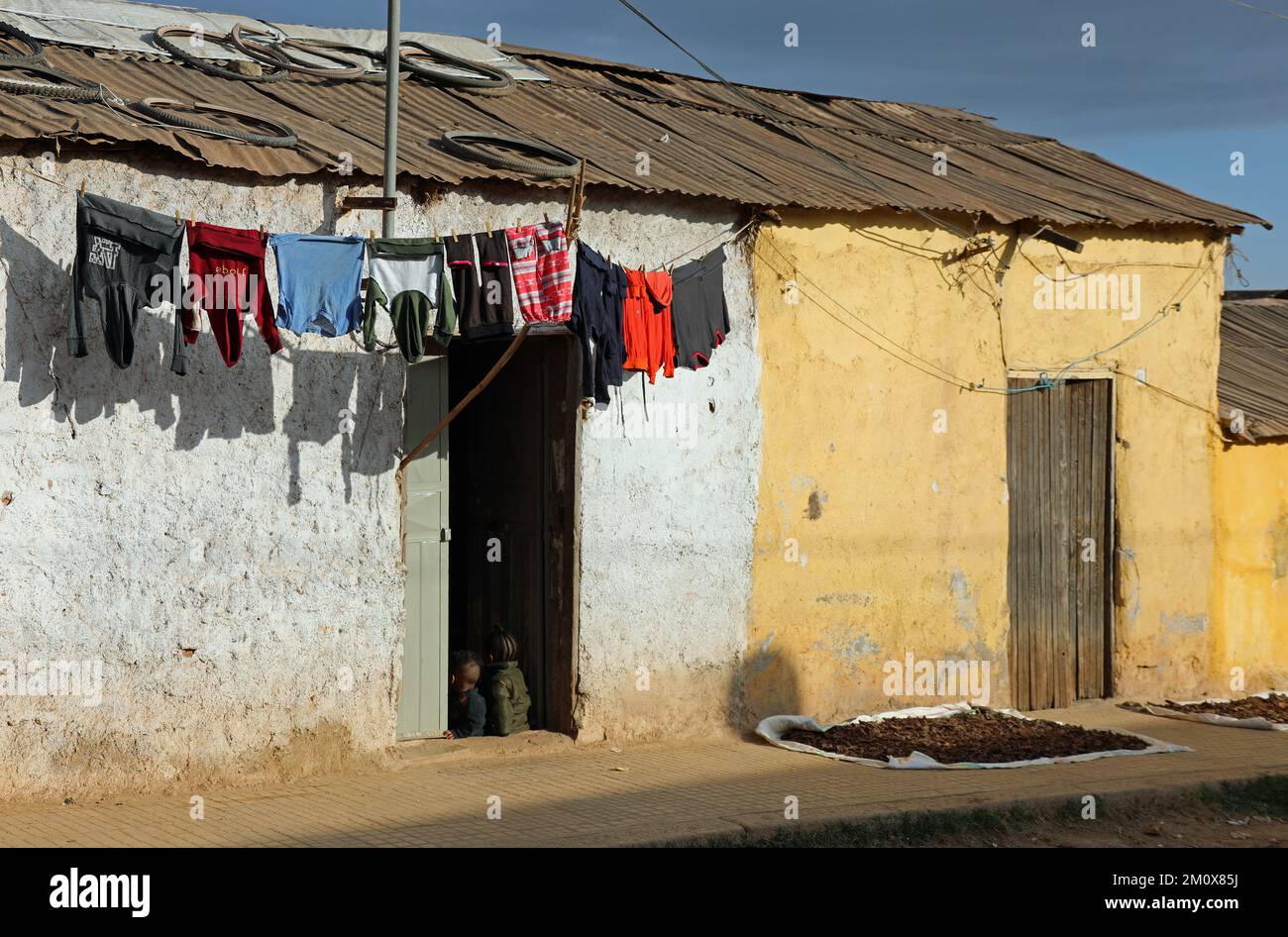 Traditionelles Haus am Stadtrand von Asmara mit Kindern, die in der Tür sitzen und sich zum Trocknen waschen hingen Stockfoto