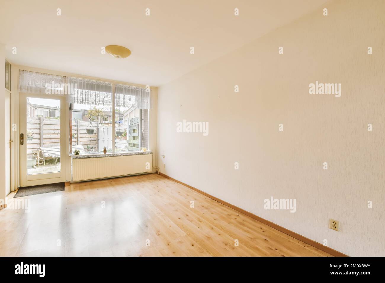 Ein leeres Wohnzimmer mit Holzfußboden und weißen Wänden, es gibt eine Tür in der Ecke rechts Stockfoto