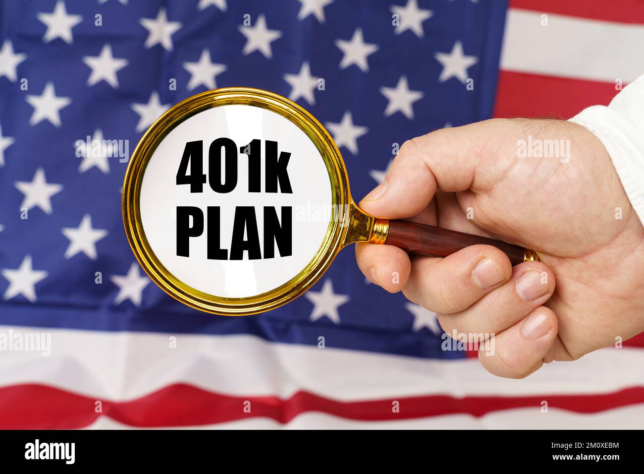 Vor der amerikanischen Flagge hält ein Mann eine Lupe in der Hand mit der Inschrift - 401K-PLAN. Stockfoto Vor der amerikanischen Flagge hält ein Mann eine Lupe in der Hand mit der Inschrift - 401K-PLAN. Stockfoto