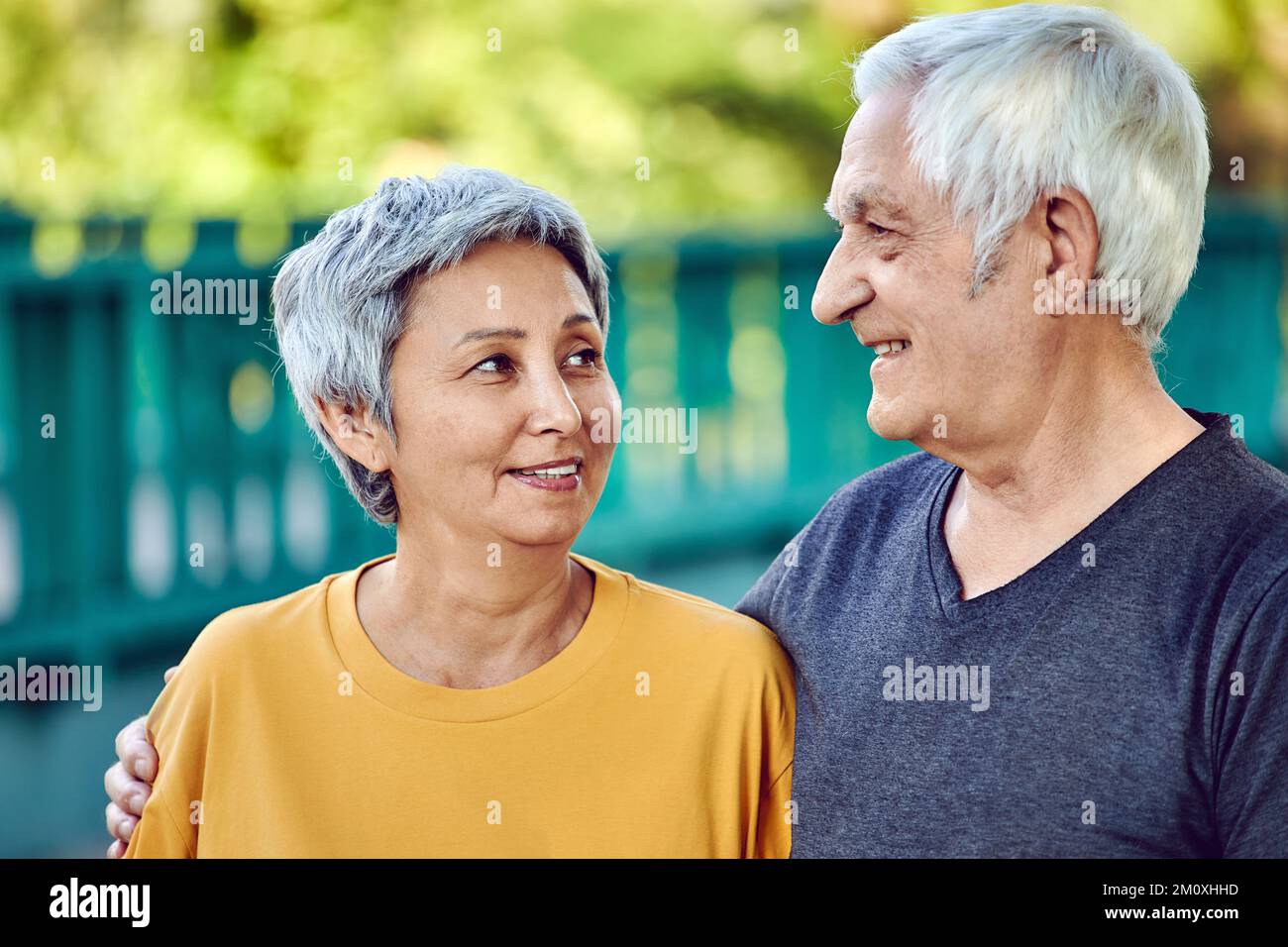 Optimistisch attraktive, multiethnische ältere 60s sportliche Paare posieren im Park und schauen einander mit Zärtlichkeit und Liebe an. Glückliche Ehe Stockfoto