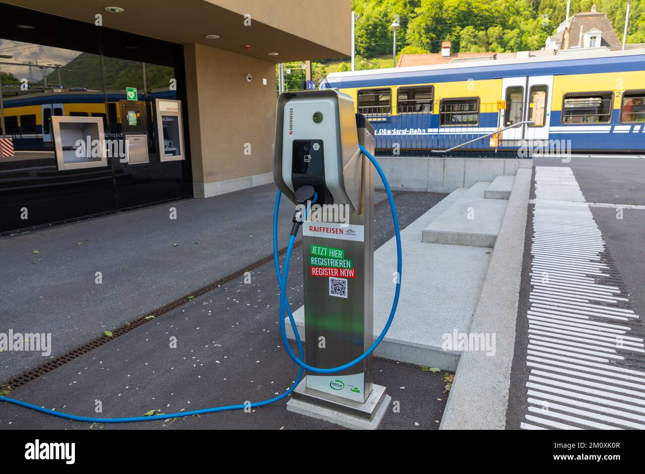 Ladestation für Elektrofahrzeuge am Bahnhof Interlaken Ost mit einer Berner Oberland-Bahn im Hintergrund. Stockfoto