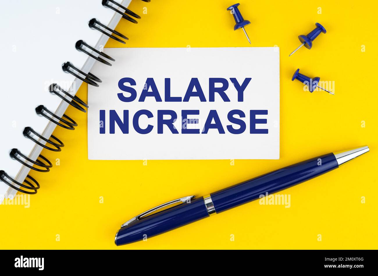 Geschäfts- und Finanzkonzept. Auf gelbem Hintergrund befinden sich ein Notizbuch, ein Stift und eine Visitenkarte mit der Aufschrift - GEHALTSERHÖHUNG Stockfoto
