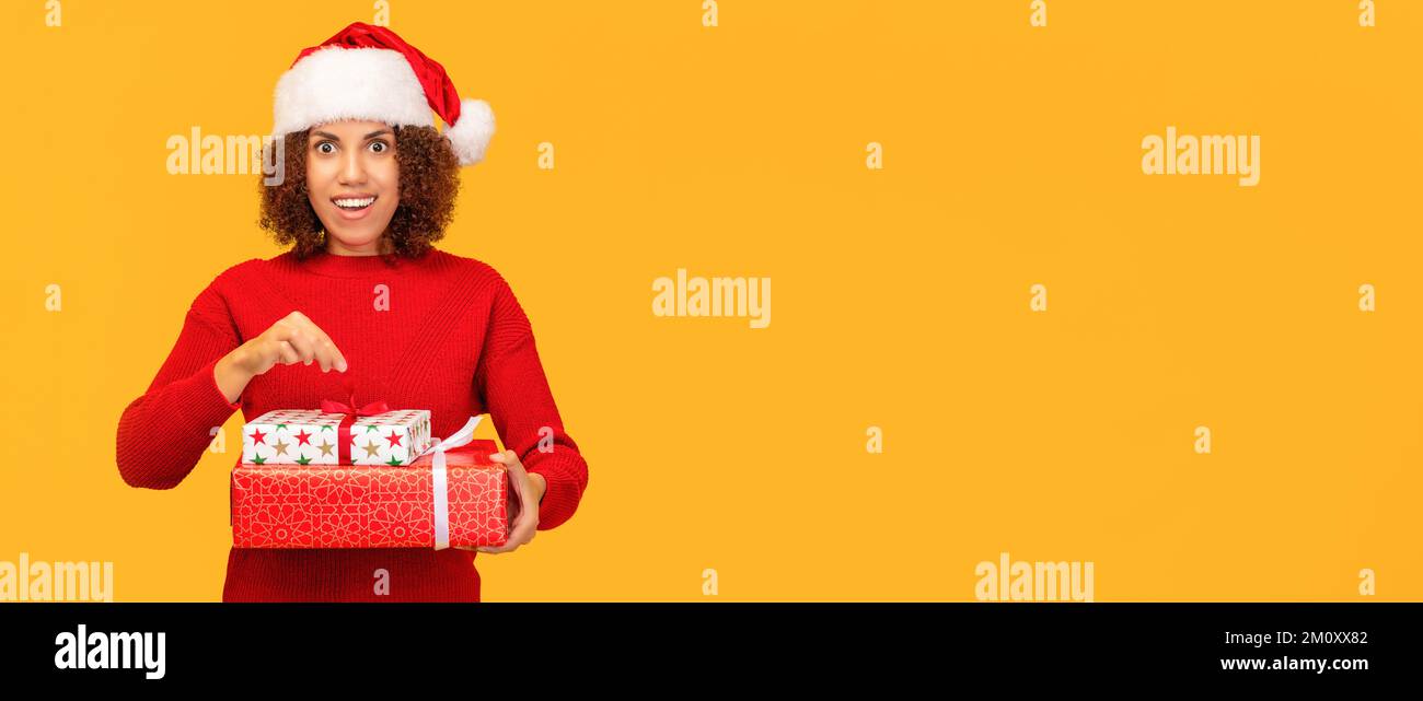 Angenehm aufgeregte glückliche Frau hält ein weihnachtsgeschenk in Händen. Eine afroamerikanische Frau mit weihnachtsmann-Hut Stockfoto