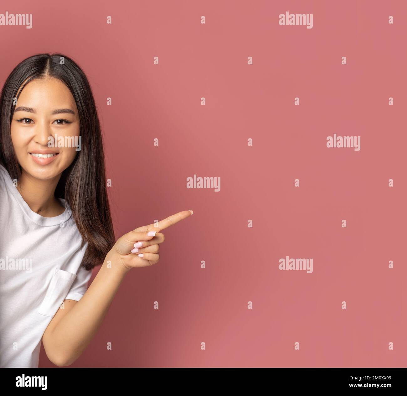 Frau lächelt mit dem Finger auf pinkfarbenen Hintergrund mit Kopierbereich, schaut in die Kamera und lächelt freundlich Stockfoto