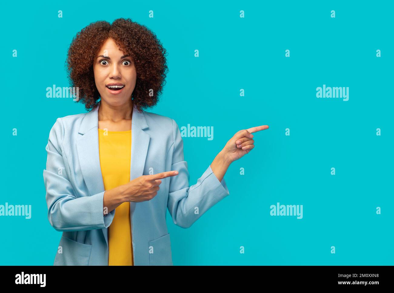 Eine afroamerikanische Büroangestellte in einer Jacke, die auf leeren Werbespot zeigt, isoliert auf blauem Hintergrund, Kopierraum Stockfoto