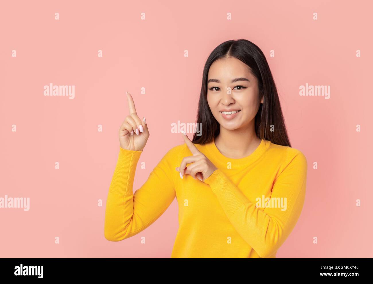 Schöne junge Frau, die lächelt, mit dem Finger auf pinkfarbenen Hintergrund zeigt, mit Platz zum Kopieren, lächelt freundlich Stockfoto