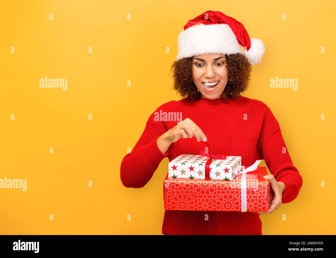 Angenehm aufgeregte glückliche Frau hält ein weihnachtsgeschenk in Händen. Frau mit weihnachtsmann-Hut auf orangefarbenem Hintergrund, lächelnd Stockfoto