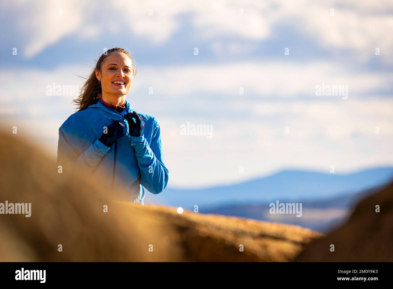 Eine Frau in einer blauen Jacke, die in den Bergen lächelt Stockfoto