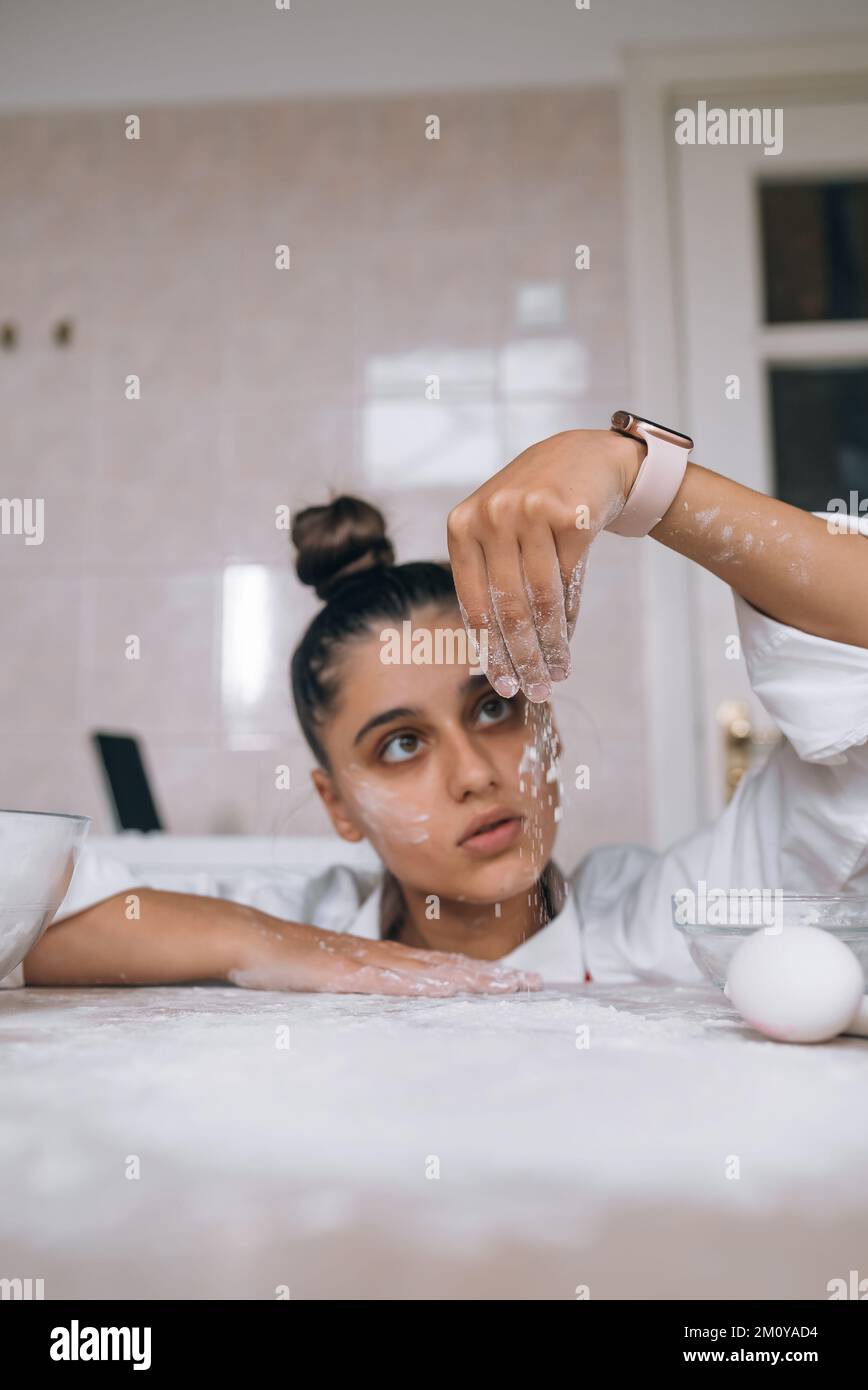 Müde junge Frau gießt Mehl auf den Küchentisch Stockfoto