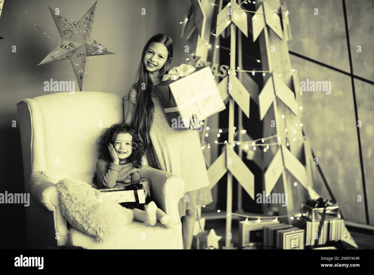 Zwei kleine Mädchen mit Geschenken stehen neben einem stilisierten Weihnachtsbaum. Schwarzweißfoto Stockfoto