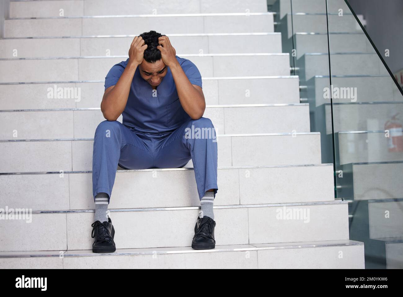 Ich fühle mich, als würde ich den Verstand verlieren. Ein junger männlicher Arzt, der weint, während er in einem modernen Krankenhaus arbeitet. Stockfoto