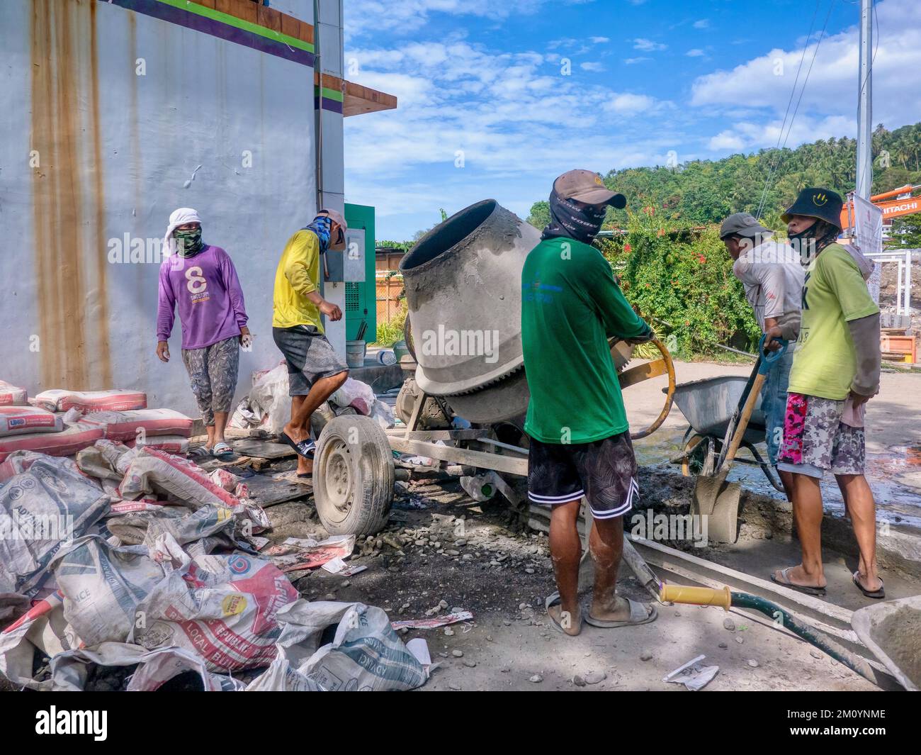 Puerto Galera, Philippinen - 9. April 2022: Philippinische Arbeiter, die einen tragbaren Betonmischer auf einer Baustelle auf der Insel Mindoro verwenden. Stockfoto