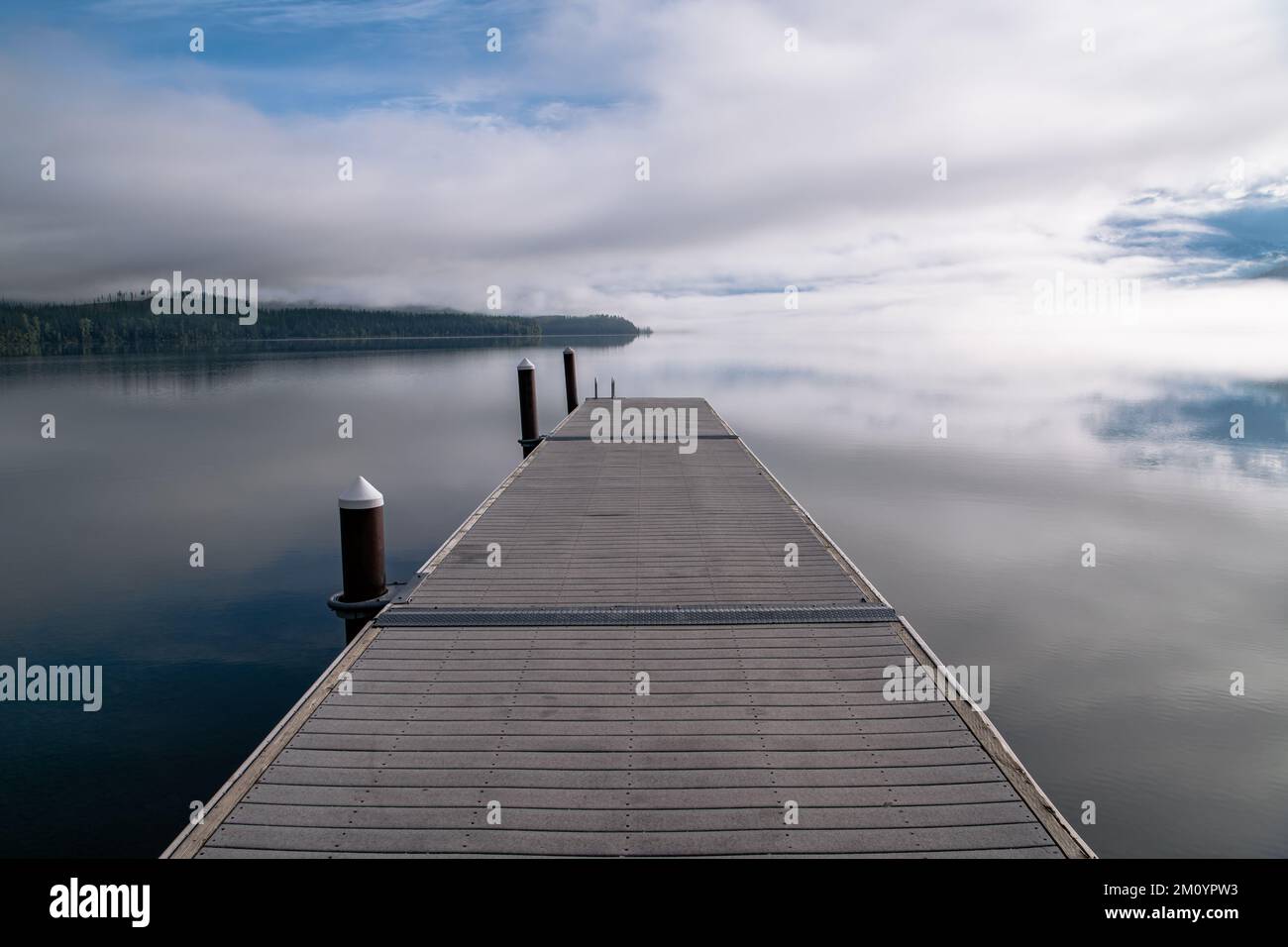 Ausblick auf die Bootsanlegestelle über dem ruhigen See mit blauem Himmel, Wolken und Nebel am Lake McDonald, Glacier National Park, Montana Stockfoto