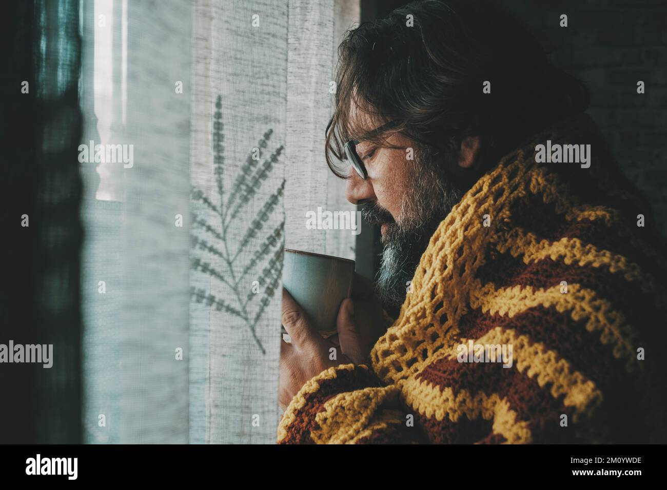 Ein Mann, der zu Hause kalte Temperaturen erlitten hat, um Gas zu sparen, Energie zu sparen und Preise zu zahlen. Seitenansicht männlicher Gäste, die Kaffee oder Tee trinken. Aufblasen Stockfoto
