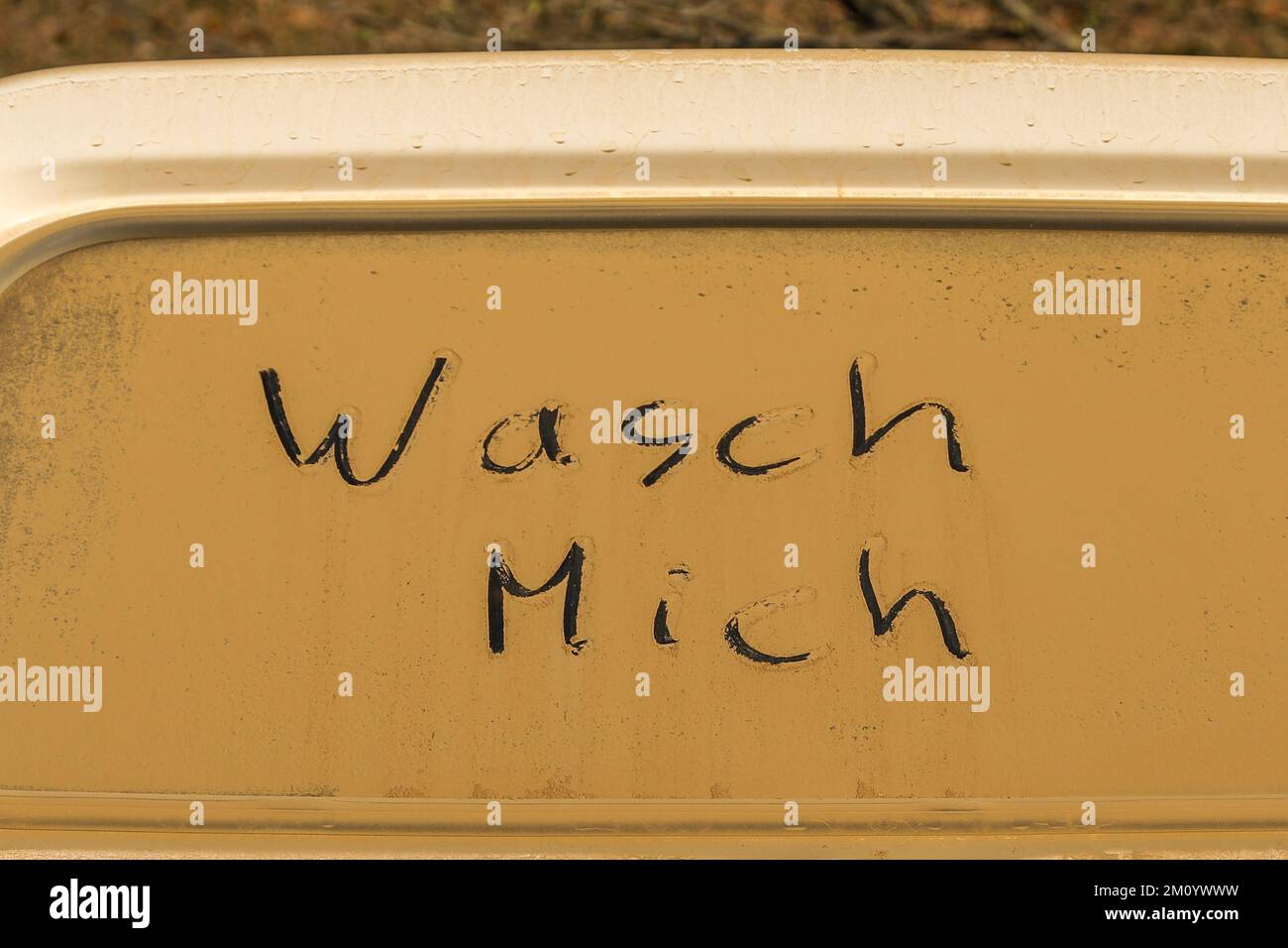 Die deutschen Wörter 'wasch mich' (Wasch mich) stehen auf einem dreckigen (orangefarbenen Sand) Fenster eines Autos Stockfoto