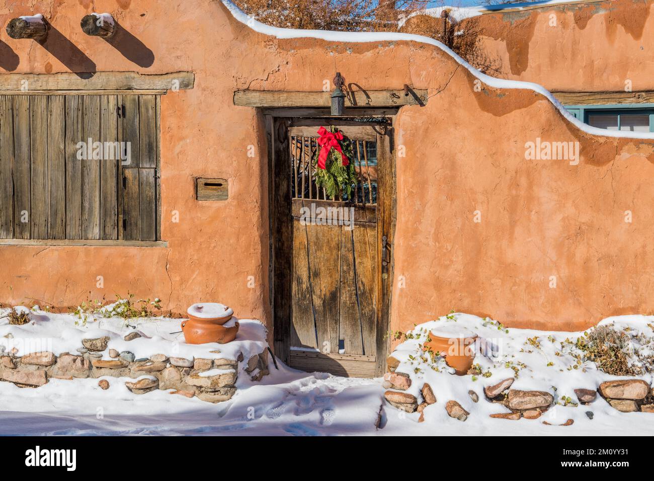 Verschneite Winterszene mit Weihnachtskranz auf einer rustikalen Holztür in der lehmwand in Santa Fe, New Mexico Stockfoto