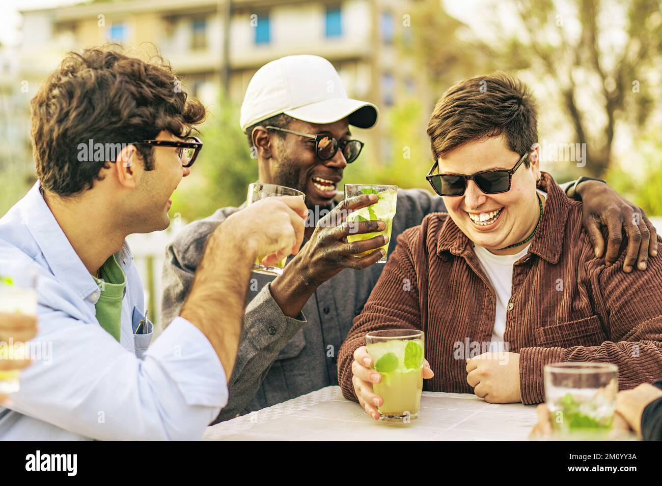 Vielfältige Gruppe von 20s jungen Freunden, die im Pub Cafe im Freien scherzten und lachten - multiethnische junge Leute, die im Tter sitzen und Mojito-Cocktails trinken Stockfoto