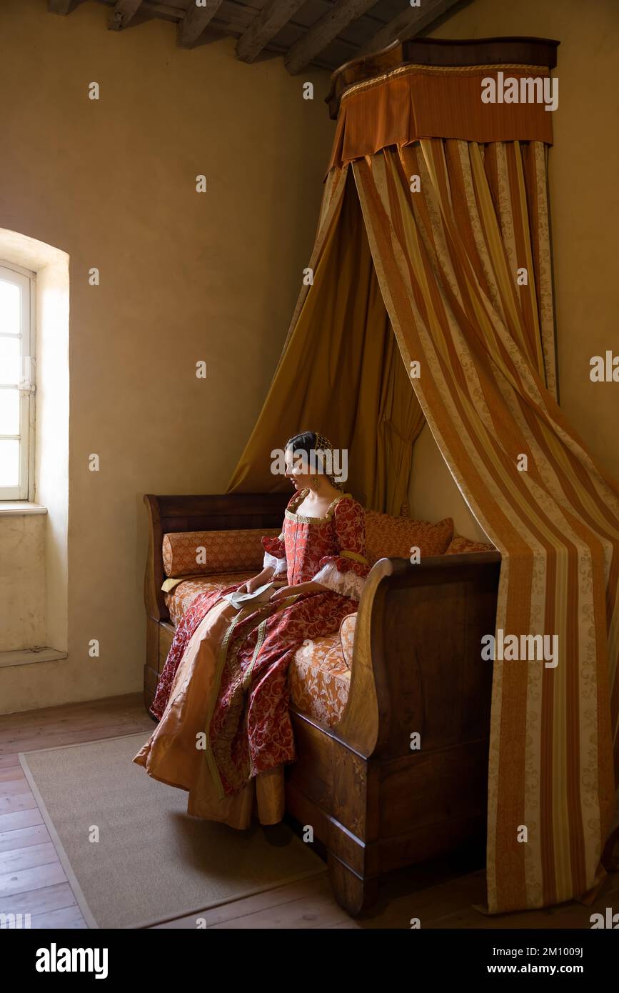 Renaissance-Dame in spätmittelalterlichem Kleid sitzt auf einem schönen Himmelbett in ihrem Schloss Schlafzimmer Stockfoto