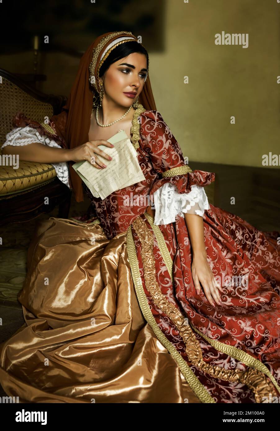 Junge Frau in mittelalterlichem Renaissance-Kostüm und französischer Kapuze, die mit einem Brief auf dem Boden sitzt Stockfoto