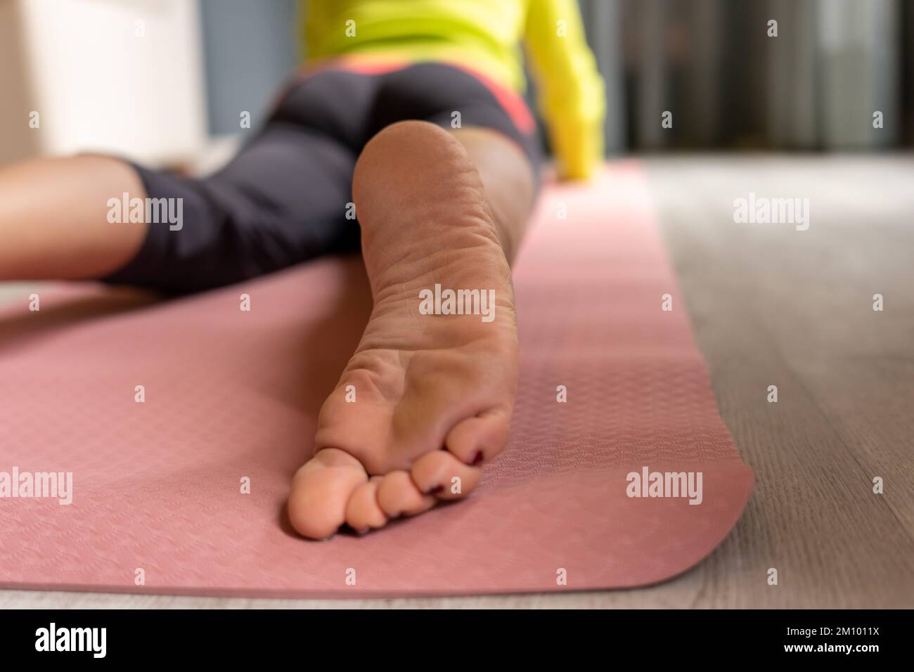 Bodenebene der unerkennbaren Ernte barfuß liegend auf der Matte während des Yoga-Trainings zu Hause in der Cobra-Pose Stockfoto