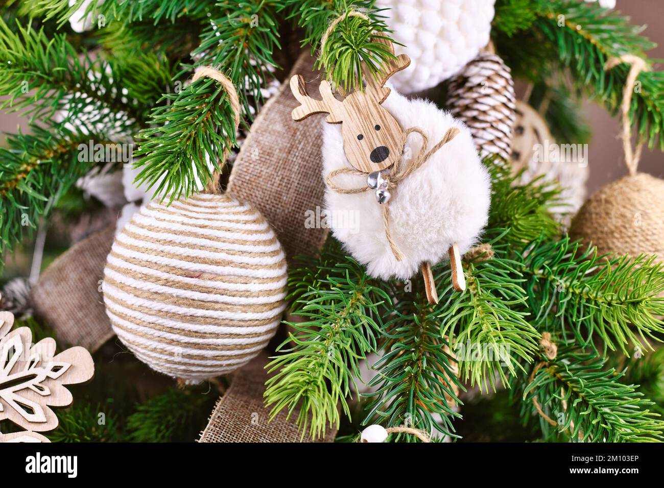 Natürliche Weihnachtsbaumschmuck aus beigefarbenem und weißem Juteseil und Schafsschmuck auf Baumzweigen Stockfoto