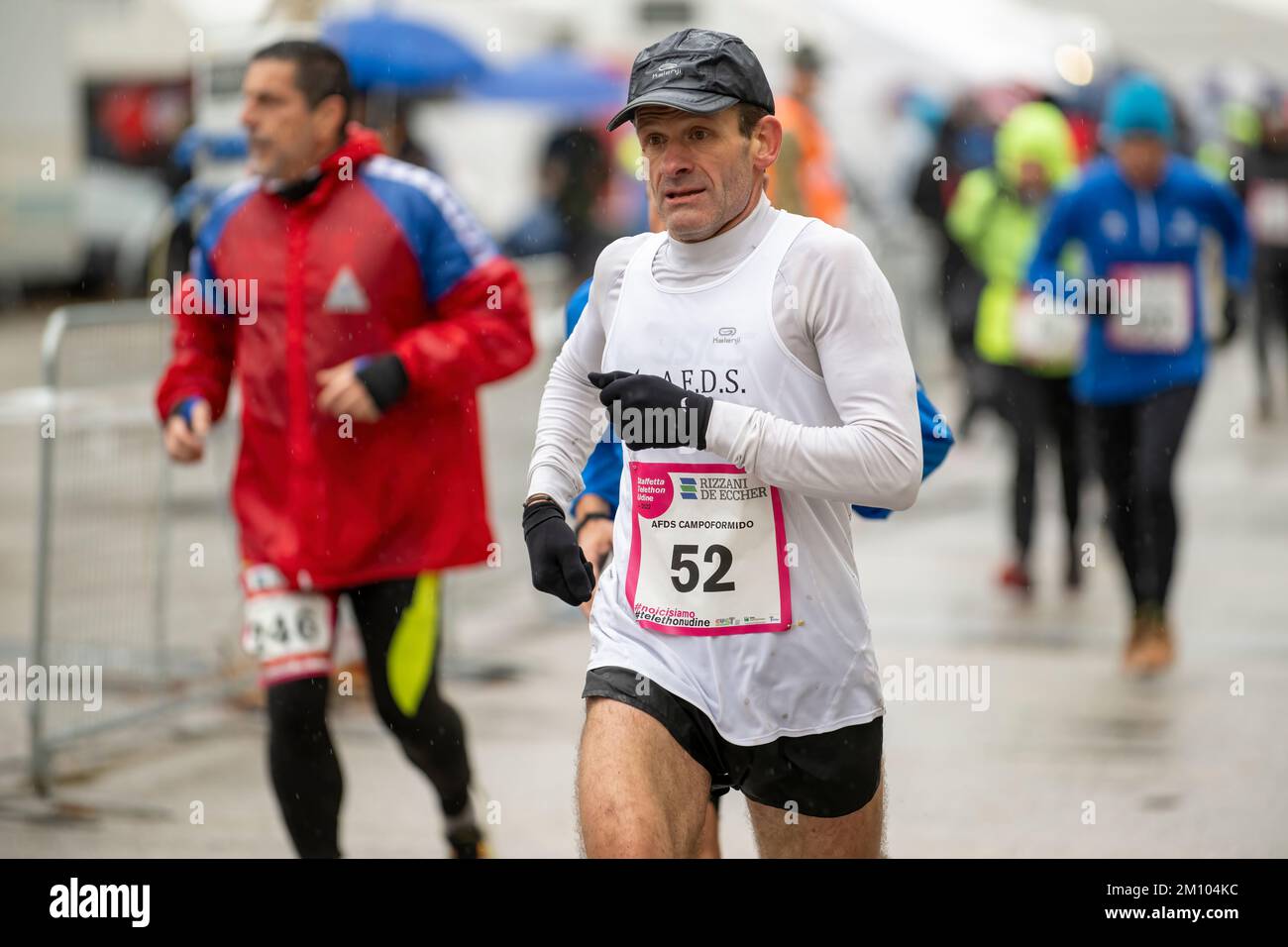 Sportler, die anlässlich des Telethon-Marathon-Staffelrennen unter Regen laufen. Udine City, Italien. 4. Dezember 2022. Stockfoto