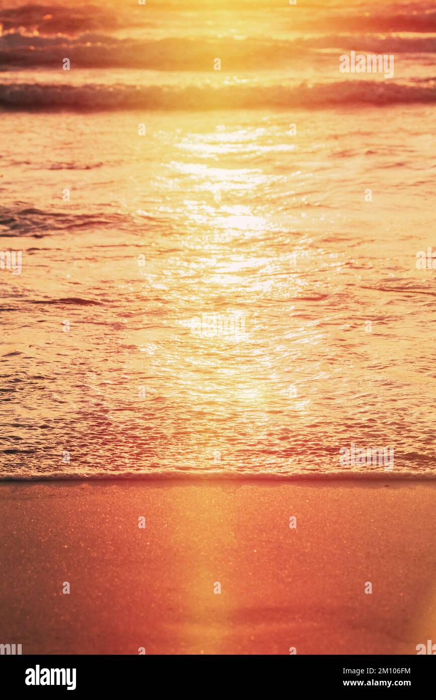 Sonnenuntergang über dem Meer. Riplpe Meer Ozean Wasseroberfläche mit kleinen Wellen. Ozean Wasser Schaum Spritzwasser waschen Sandstrand. Vertikales Foto Stockfoto