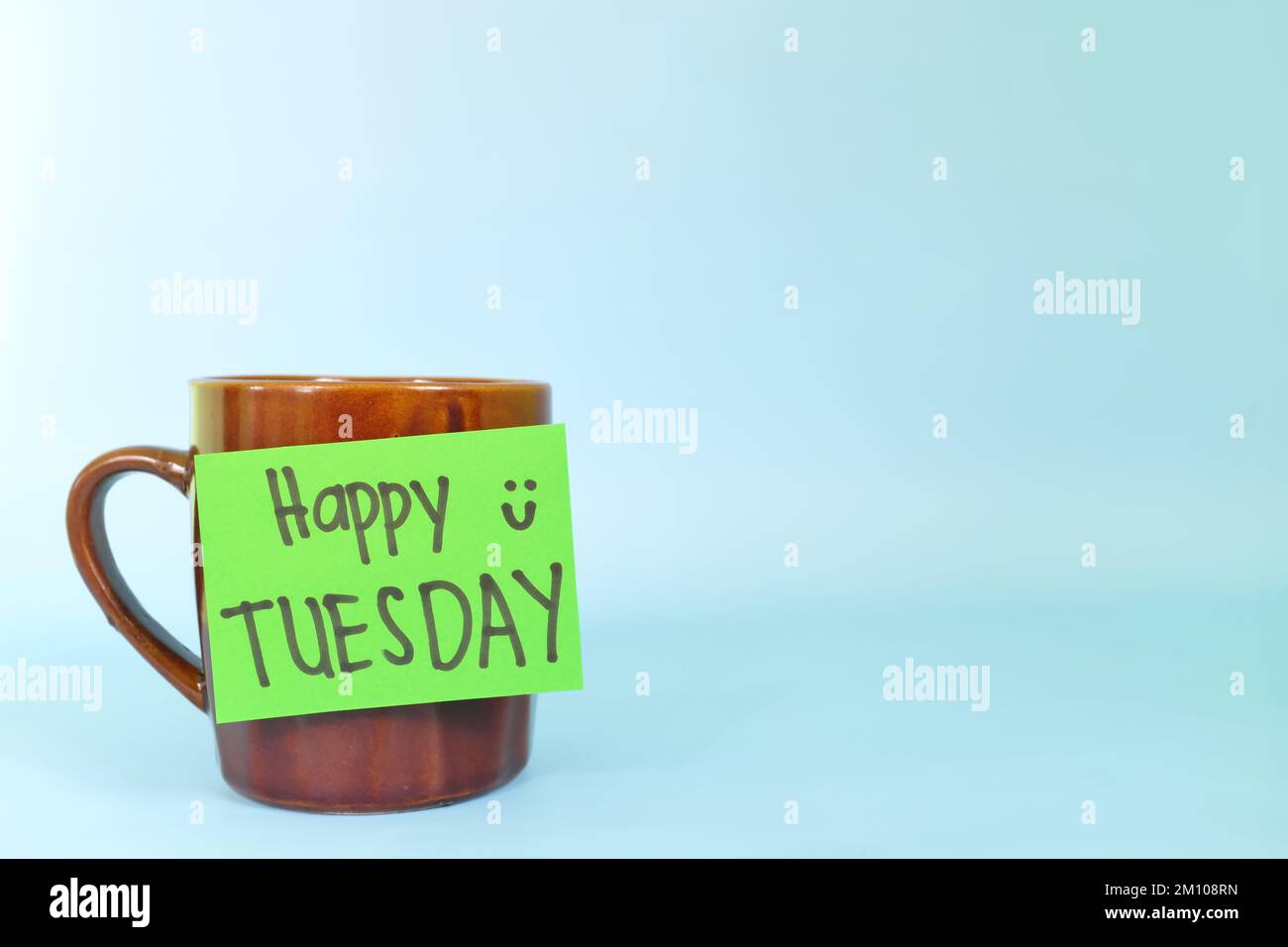Willkommen, hallo und Happy Tuesday Concept. Selektiver Fokus der Kaffeetasse mit schriftlicher Nachricht auf blauem Hintergrund. Stockfoto