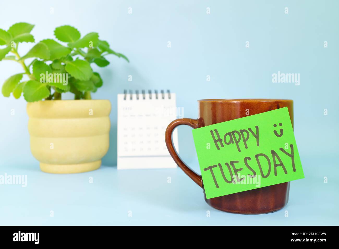 Willkommen, hallo und Happy Tuesday Concept. Selektiver Fokus der Kaffeetasse mit grünem Zettel und schriftlicher Botschaft. Stockfoto