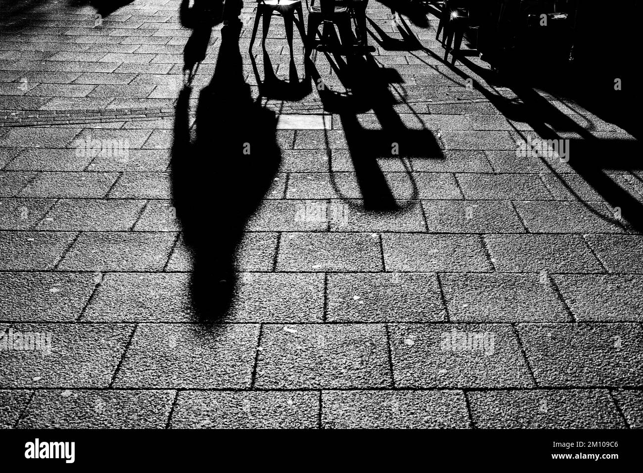 Lange Schatten von Stühlen, Tischen und Figuren in Schwarz und Weiß. Dramatische Hintergrundbeleuchtung mit Schatten, die direkt auf die Kamera zugehen. Schattenkonzept Stockfoto