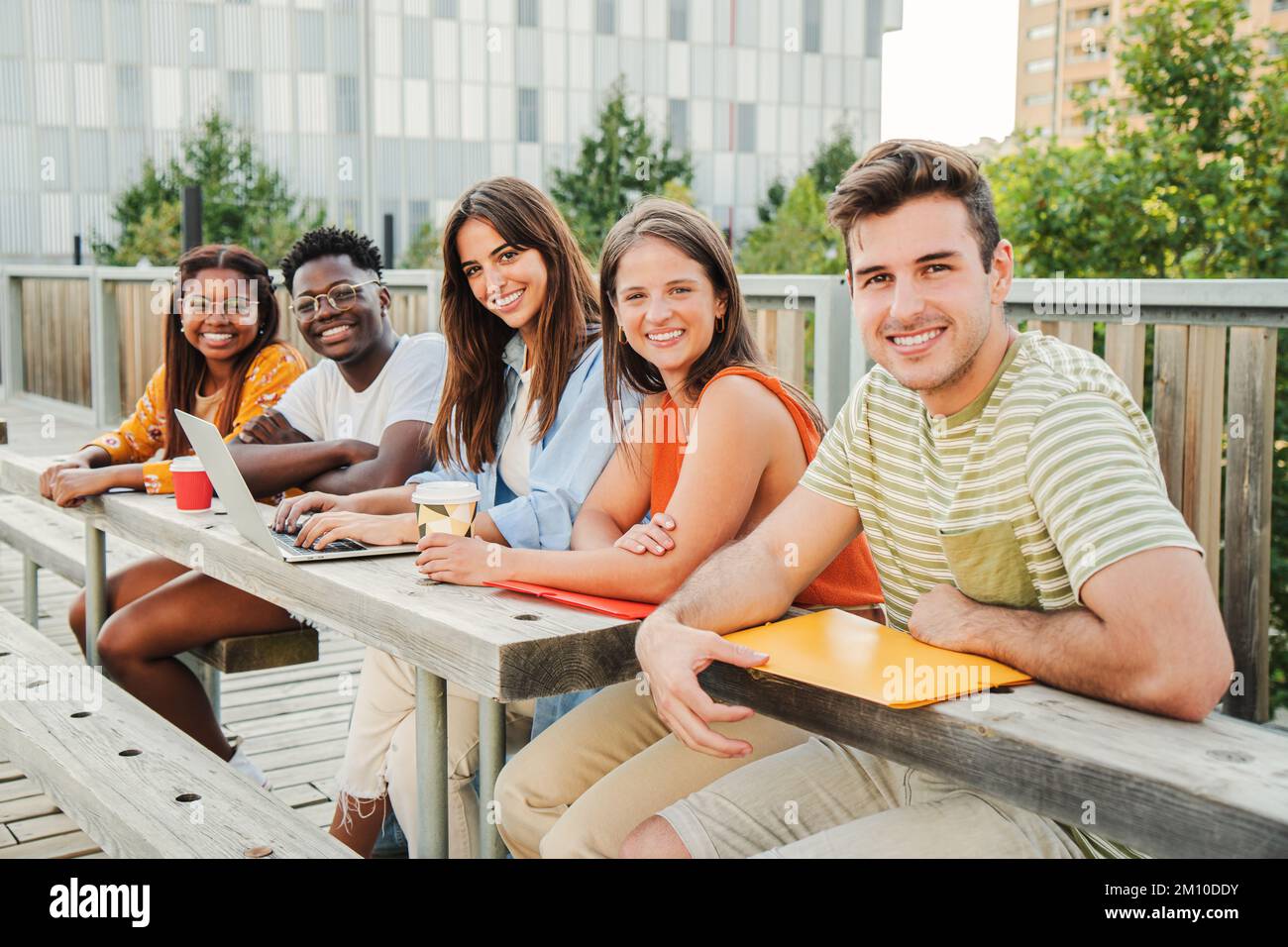 Multirassische Gruppe glücklicher Teenager, die vor der Kamera lächeln und sich vor dem Universitätscampus entspannen und eine Pause einlegen. Treffen von jungen und lustigen College-Leuten, die das Sonnenlicht genießen, lernen und posieren im Freien. Bildungskonzept. Hochwertiges Foto Stockfoto