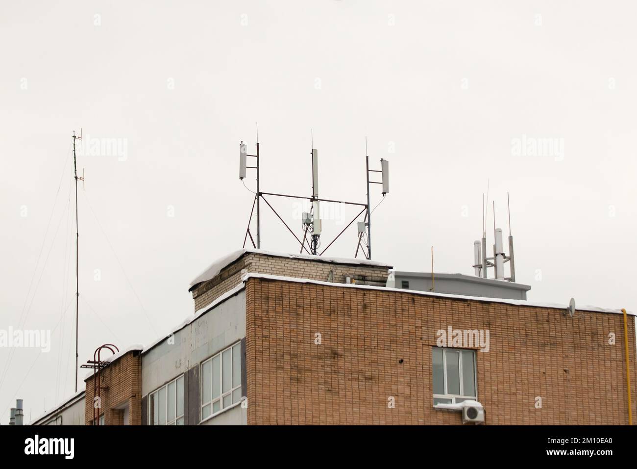 Viele verschiedene Mobilfunkantennen auf dem Dach des Hauses sorgen für Kommunikation. Schnee liegt auf dem Meilenstein, vor dem Hintergrund eines grauen Himmels. Bewölkt, kalter Wintertag, weiches Licht. Stockfoto