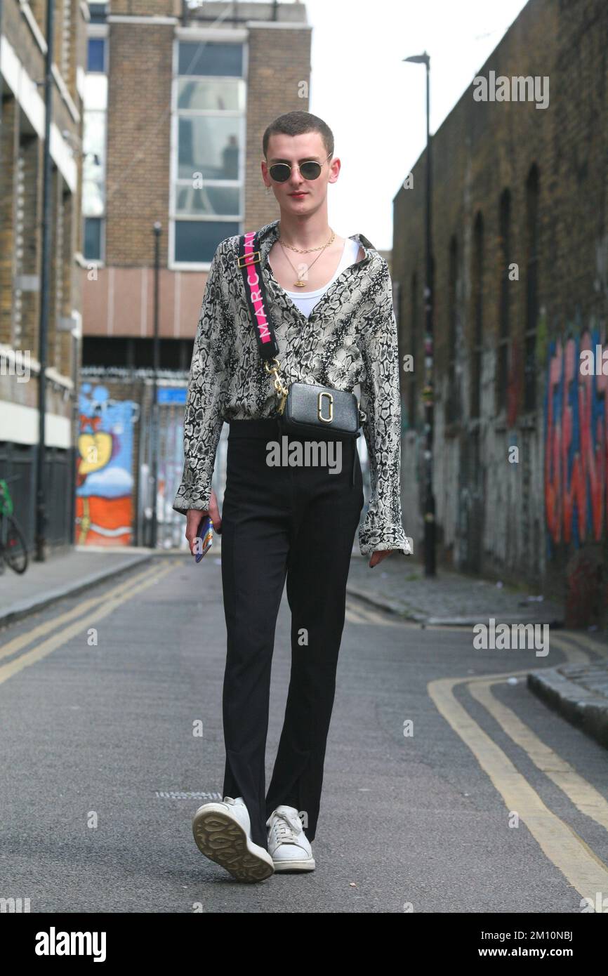 Cooles Street-Style, stylischer junger Mann mit Sonnenbrille, gemustertes Hemd, schwarze Hose und weiße Turnschuhe, die in London auf einer Straße unterwegs sind Stockfoto