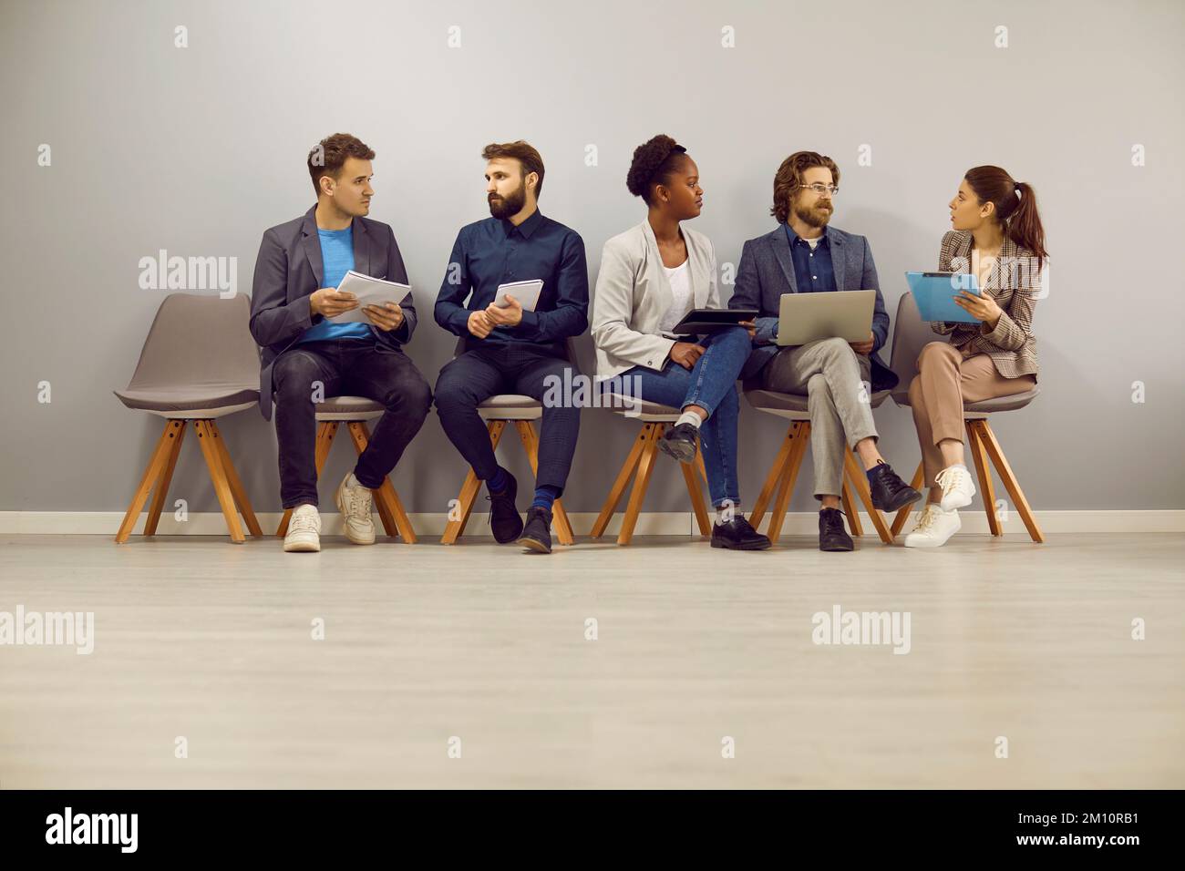 Eine vielfältige Gruppe von Personen, die sich unterhalten, während sie im Büro sitzen und auf ein Vorstellungsgespräch warten Stockfoto