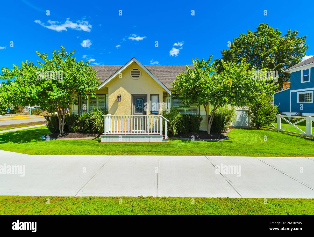 Kleines gelbes Familienhaus an sonnigen Tagen mit grünem Rasen und Betonweg Stockfoto