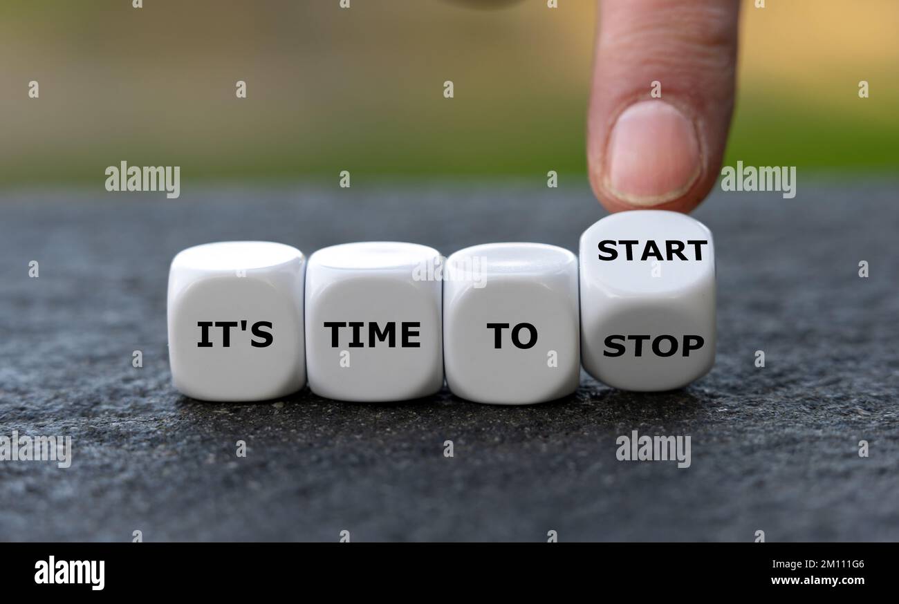 Würfeln Sie mit der Hand und ändern Sie den Ausdruck „Zeit zum Stoppen“ in „Zeit zum Starten“. Stockfoto