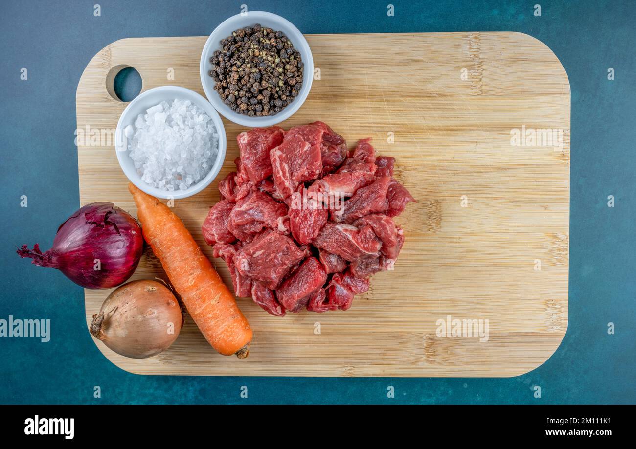 Grundlegende Rohstoffe von rohem gewürfeltem Rindfleisch, Karotten und Zwiebeln mit Gewürzen auf einem Bambusschneidbrett Stockfoto