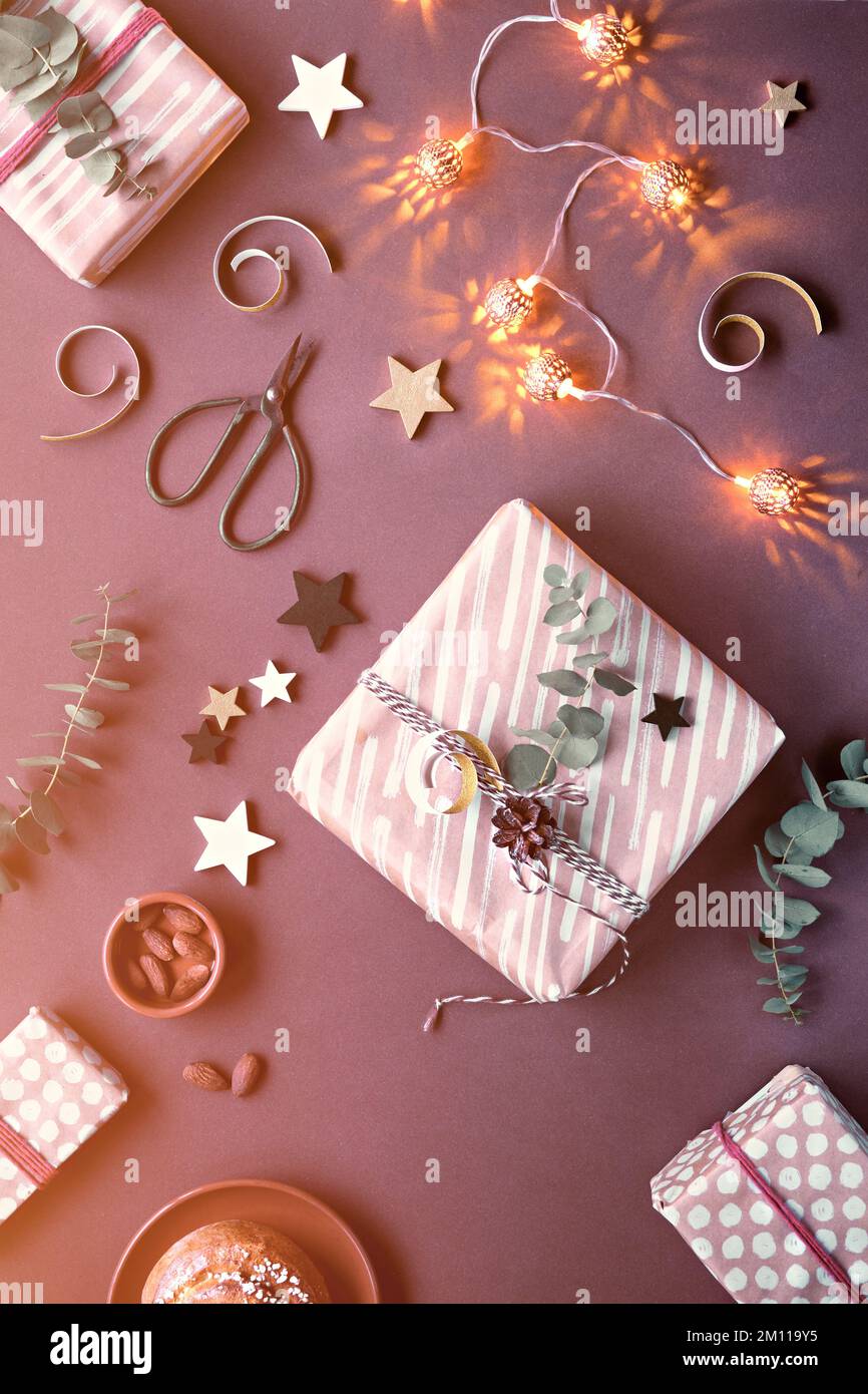 Dunkelbrauner Weihnachtshintergrund mit verpackten Weihnachtsgeschenken. Einfarbige flache Lage mit Marzipan-Süßigkeiten, Geschenkschachteln, Eukalyptus, Nüssen, Sternen Stockfoto