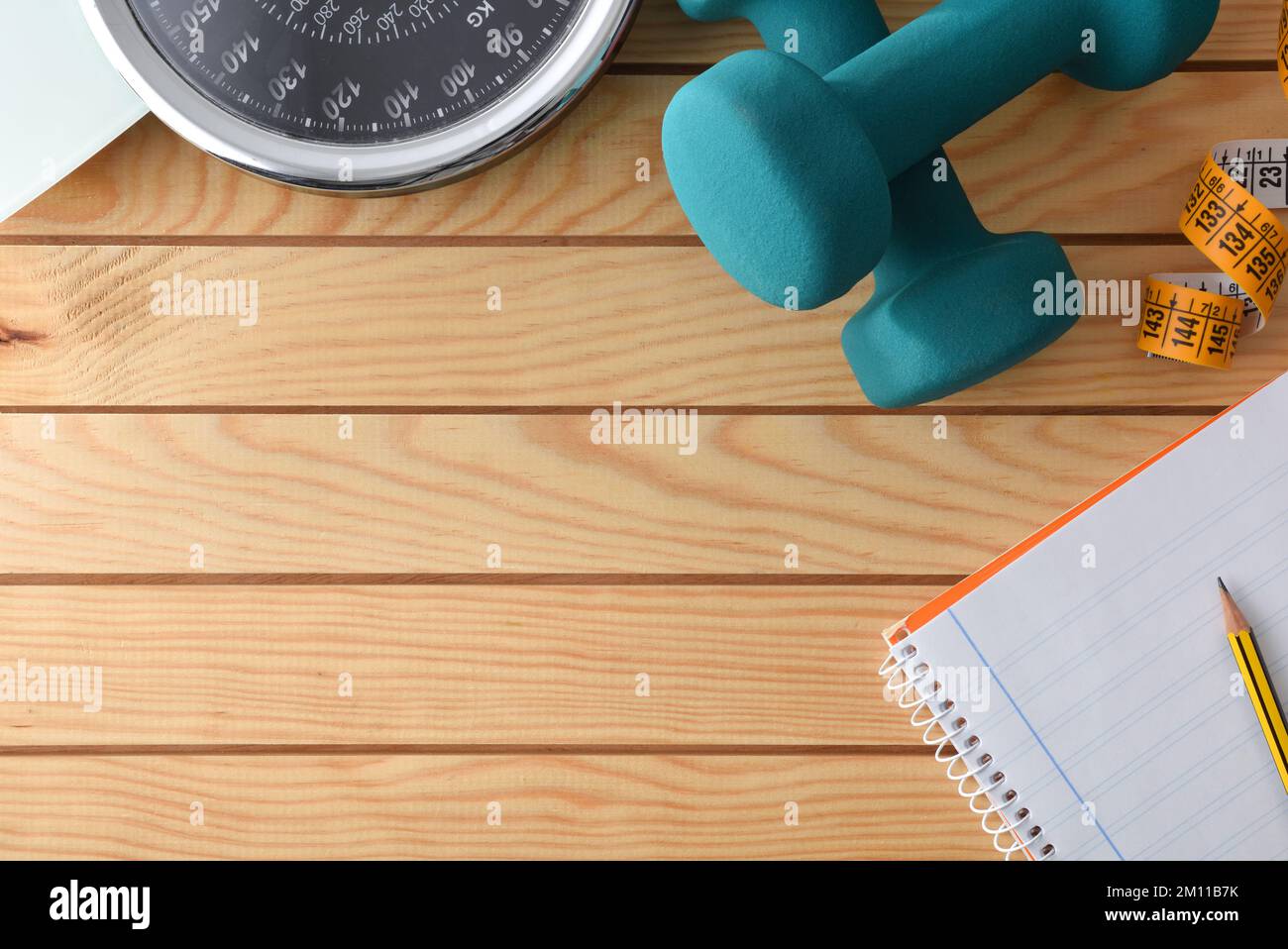 Persönlicher Trainingsplan zur Gewichtskontrolle mit Sportgeräten und Körpermessung auf einem Holztisch und Notizblock. Draufsicht. Stockfoto