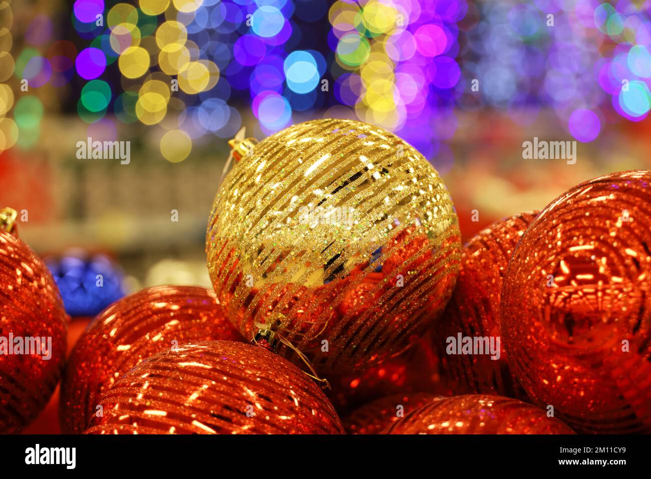 Weihnachtsspielzeug, goldene und rote Kugeln auf verschwommenem festlichem Hintergrund. Neujahrsdekoration in einem Geschäft Stockfoto