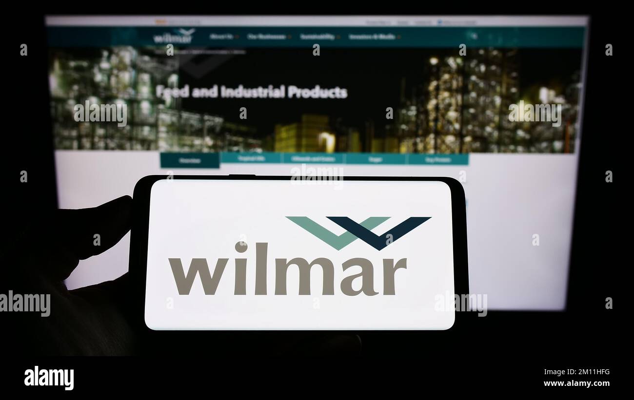 Person, die ein Smartphone mit dem Logo des singapurischen Unternehmens Wilmar International Limited auf dem Bildschirm vor der Website hält. Konzentrieren Sie sich auf das Display des Telefons. Stockfoto